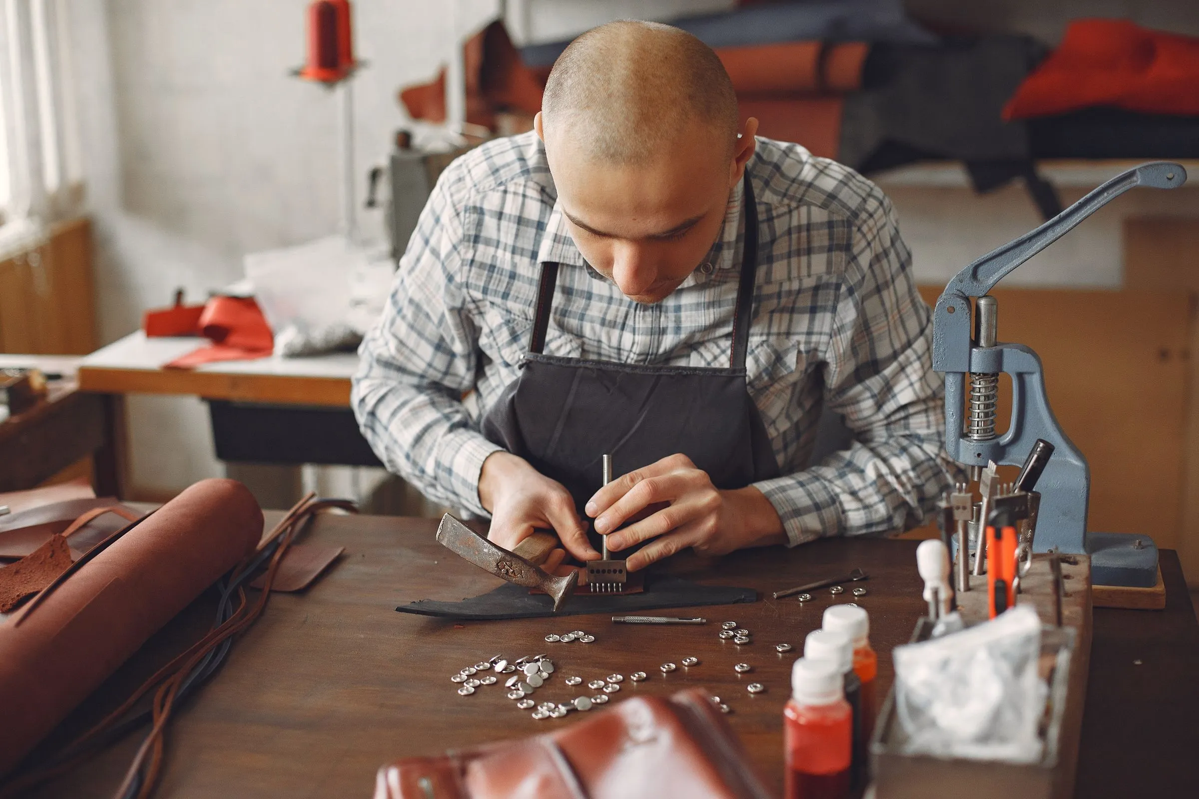 Artesano de mandil trabajando una pieza de cuero con martillo sobre su banco de taller