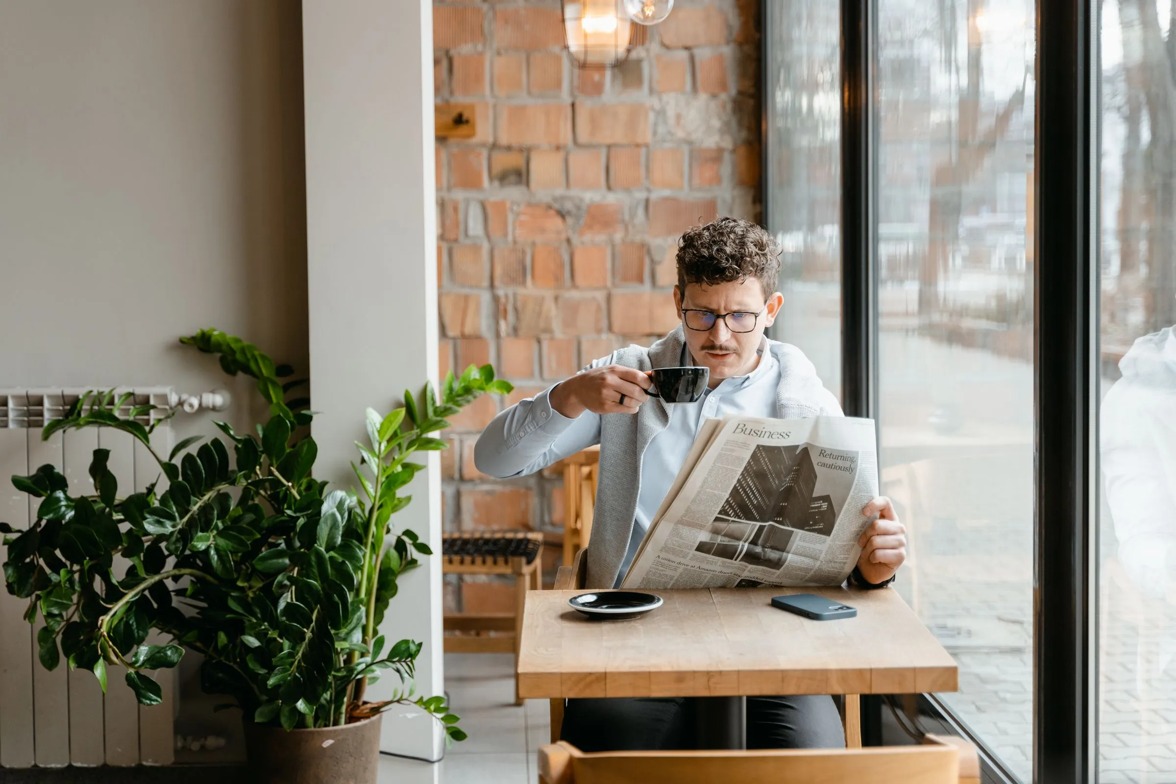 Hombre leyendo la sección de economía del periódico con un café junto a la ventana