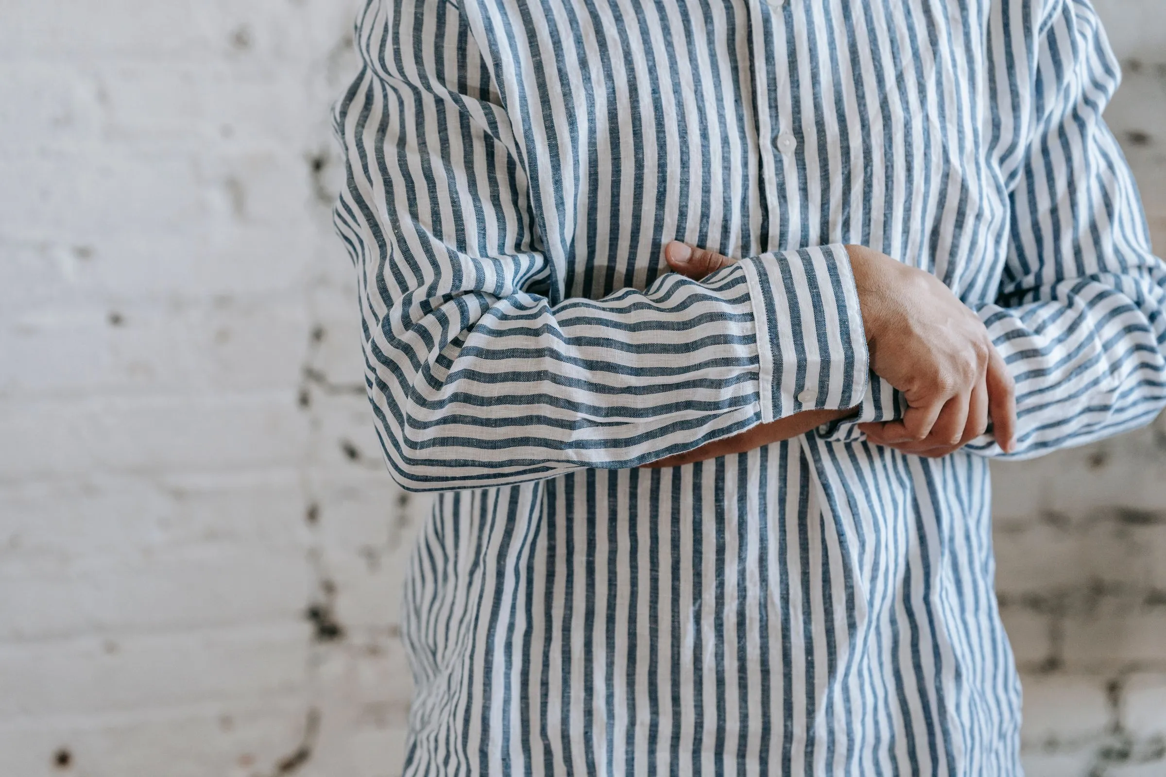 Detalle de una camisa de lino de raya azul sobre blanco, con la manga vuelta sobre el antebrazo