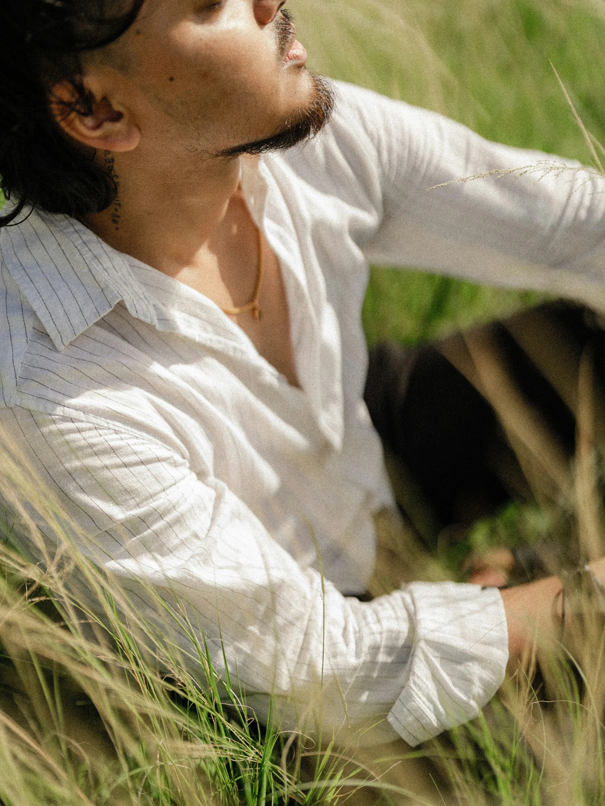 Primer plano de una camisa de lino blanco con raya finísima, con las mangas vueltas, a la luz del sol
