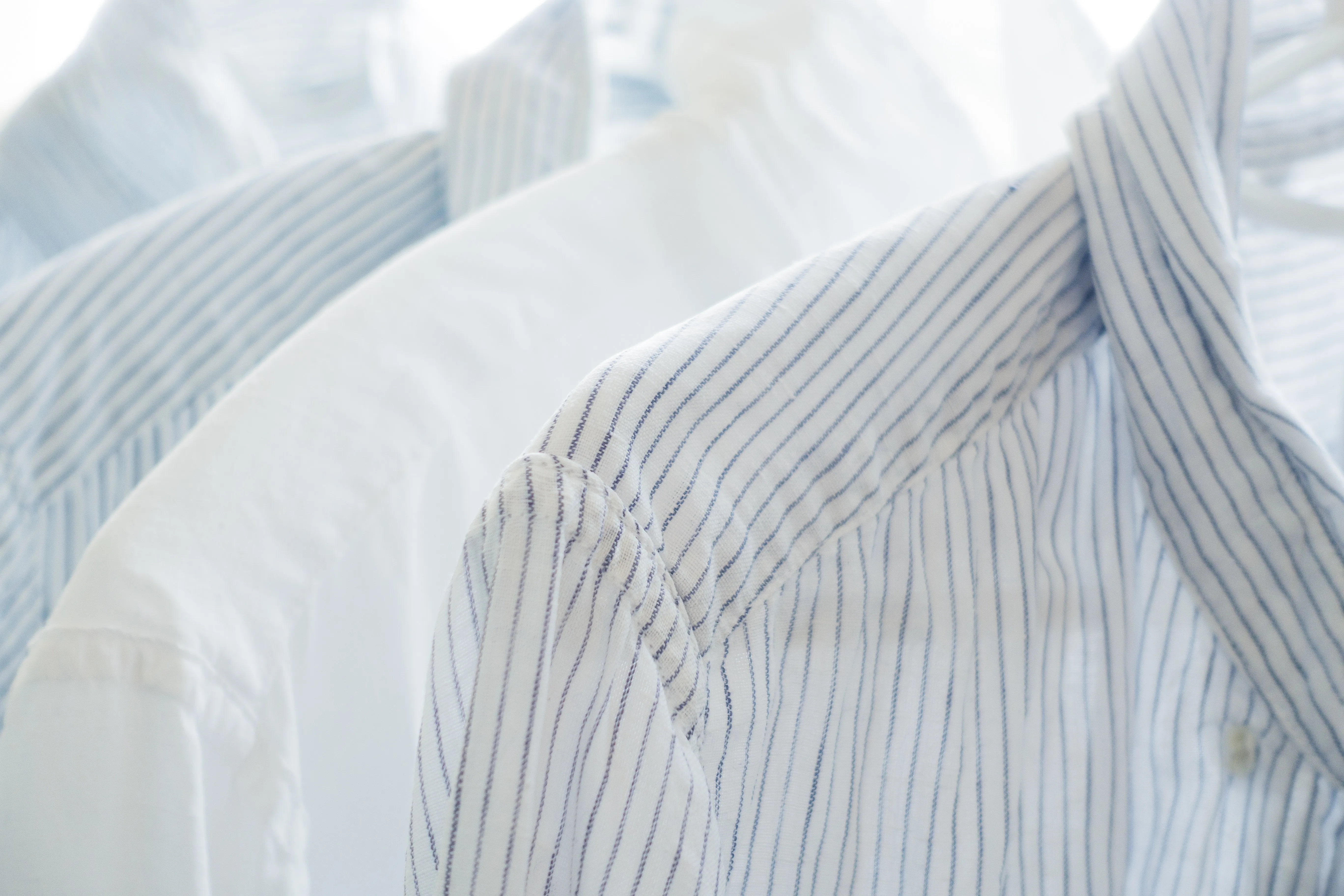 Camisa de lino blanca lisa y camisa de lino blanca de raya azul fina, colgadas a contraluz