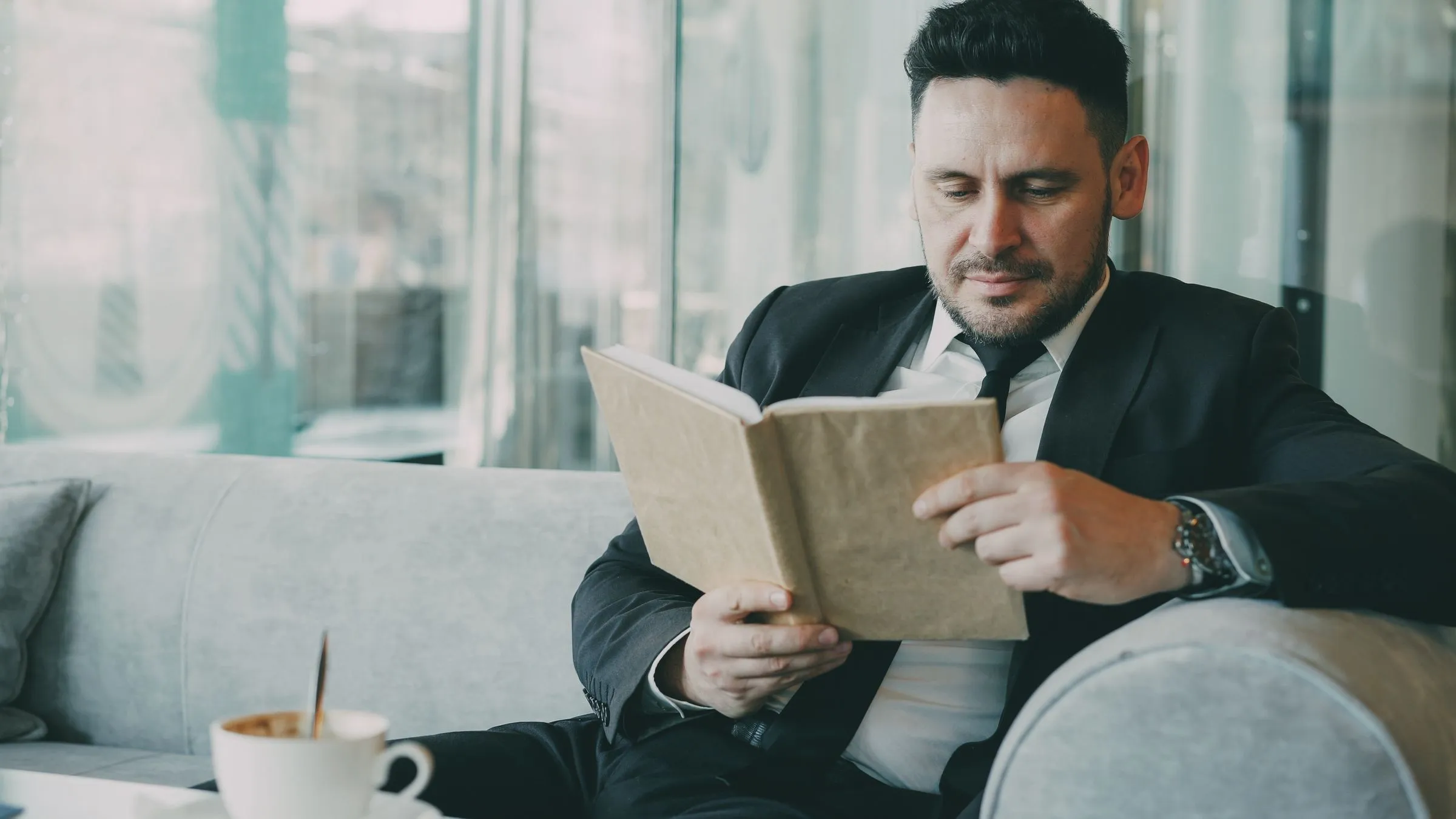 Empresario de traje leyendo un libro sentado en el salón de un café