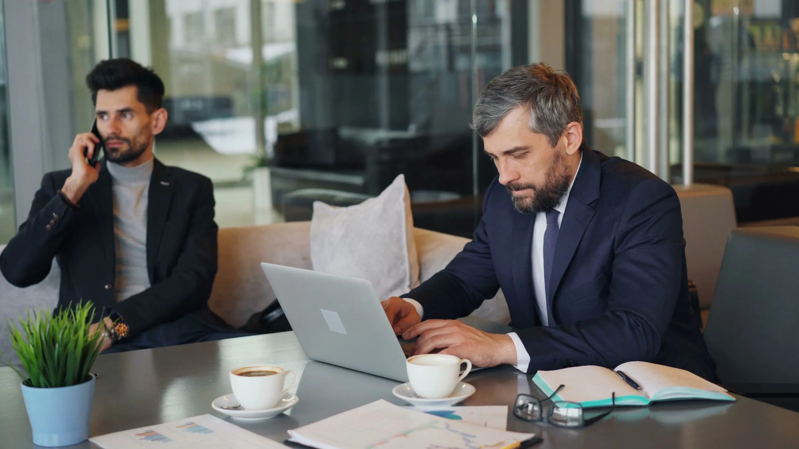 Dos hombres de negocios trabajando con portátil, café y documentos en un salón contemporáneo