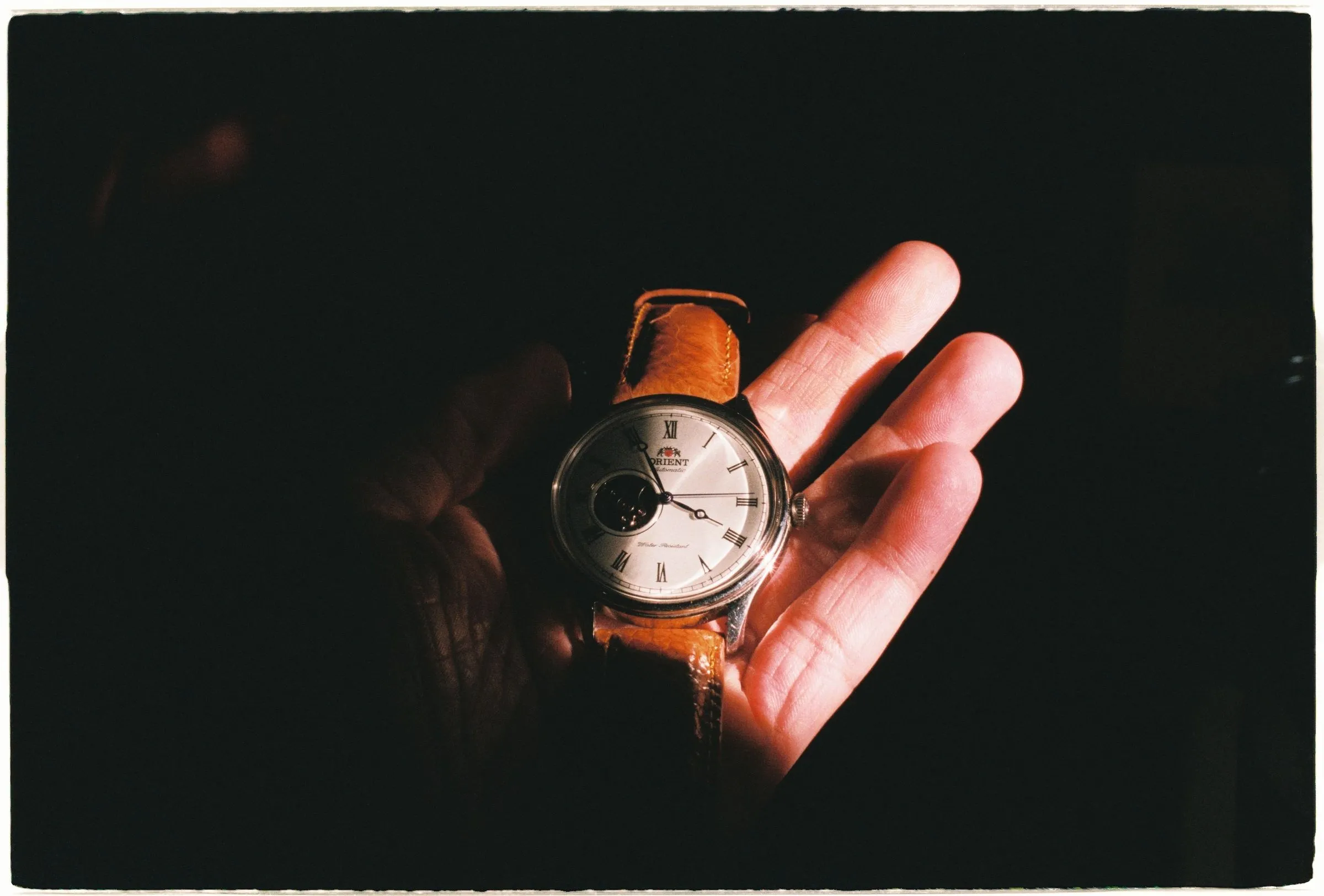 Mano sosteniendo un reloj Orient clásico de correa de piel marrón bajo una luz dramática