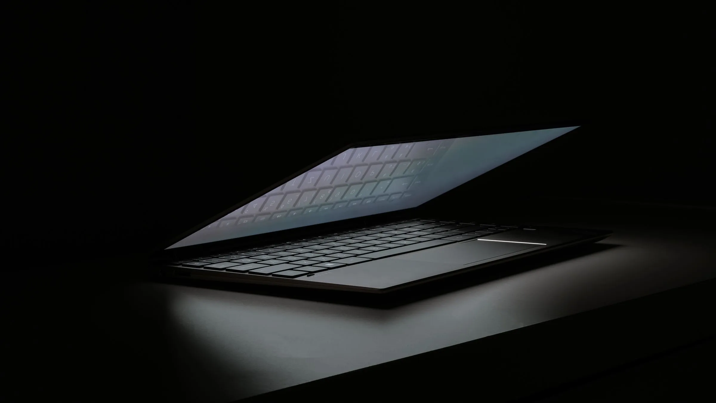 Portátil entreabierto a oscuras, con la luz de la pantalla escapando por la rendija sobre el teclado