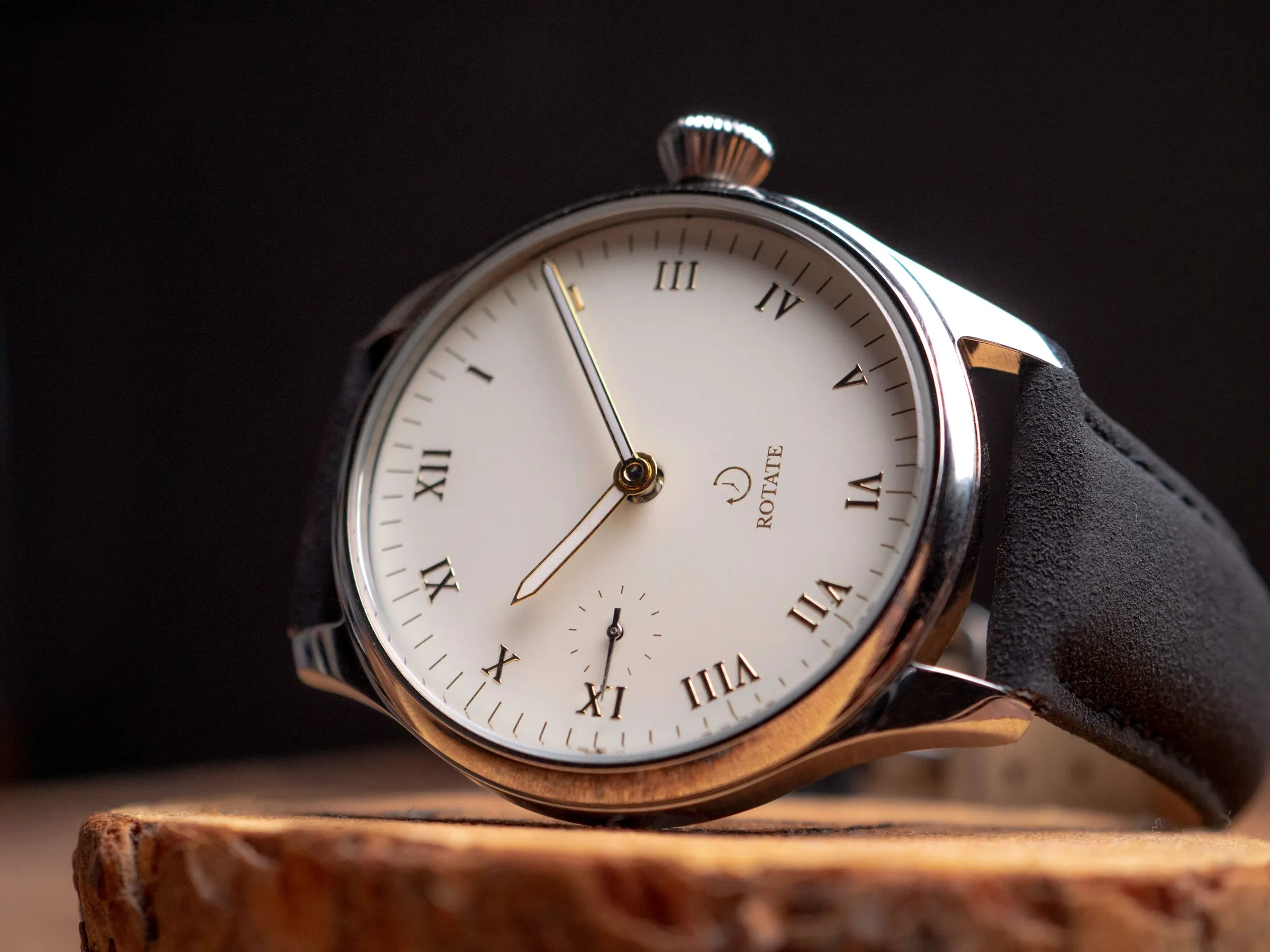 Reloj de vestir de esfera blanca con números romanos y pequeño segundero, sobre una peana de madera