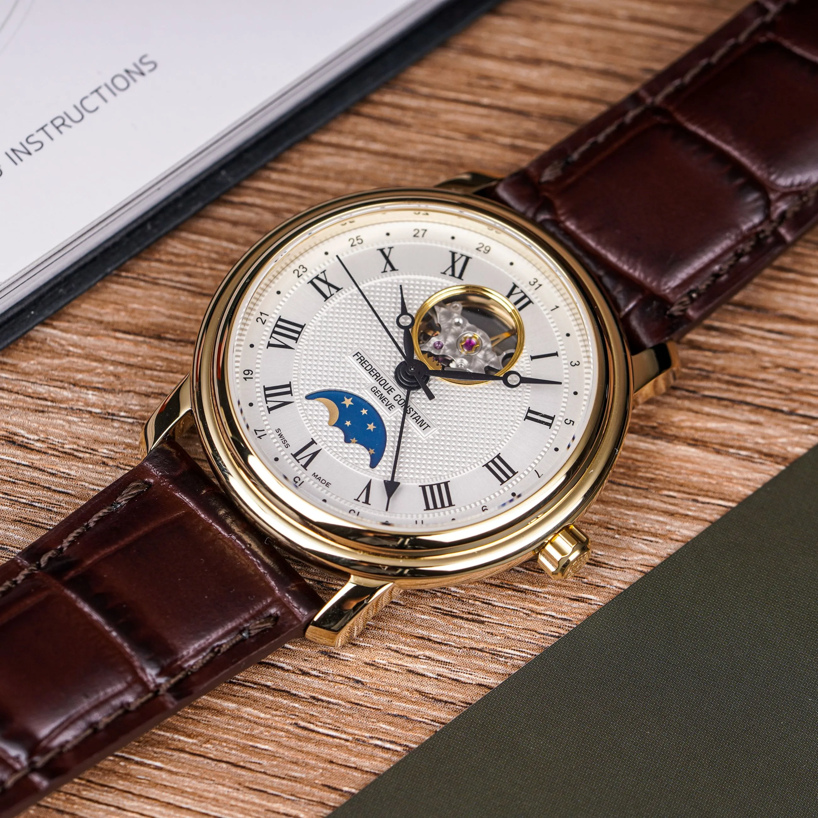 Reloj suizo dorado con esfera guilloché, fase lunar y correa de cuero marrón sobre una mesa de madera
