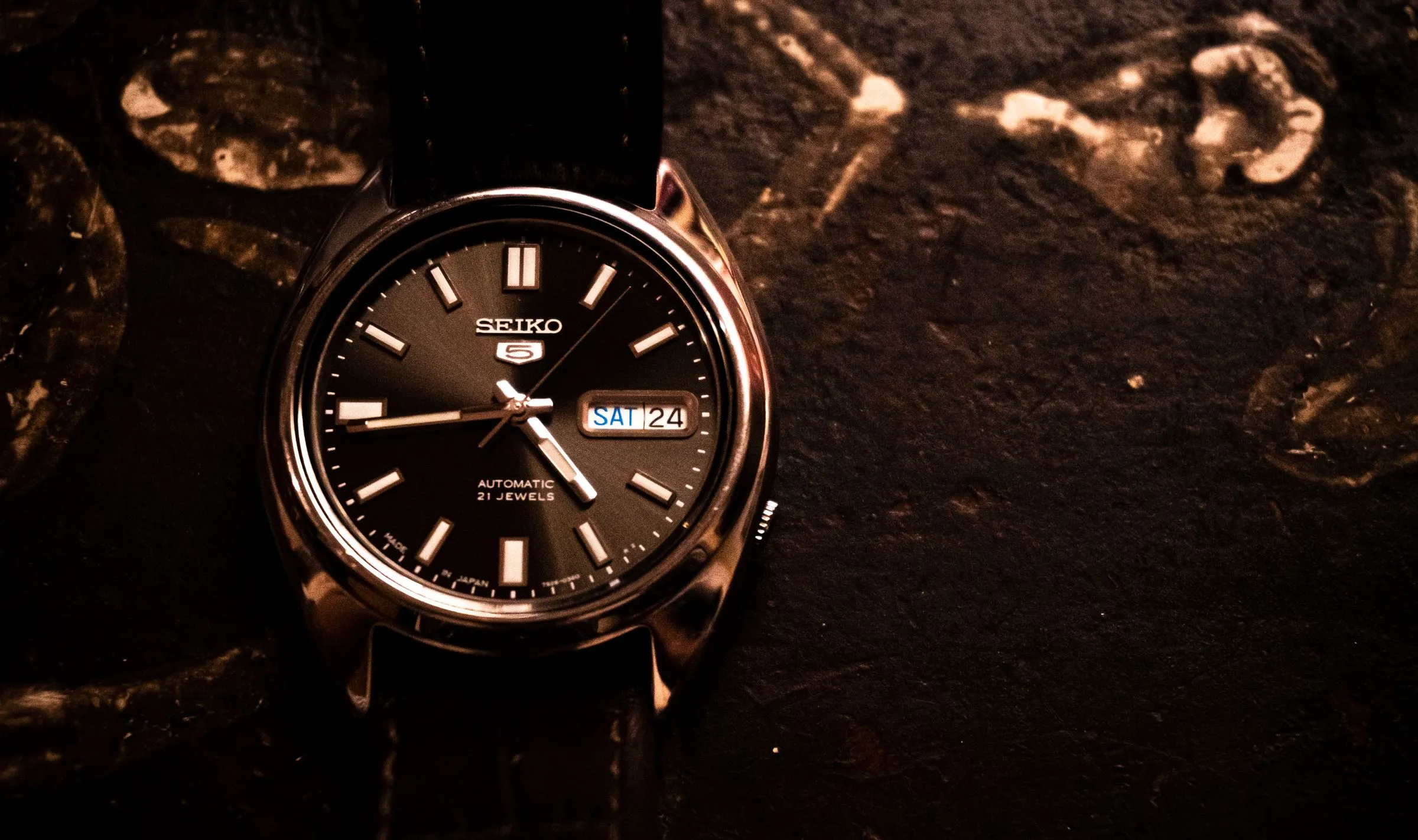 Seiko 5 automático de esfera negra con calendario sobre un fondo de piedra oscura