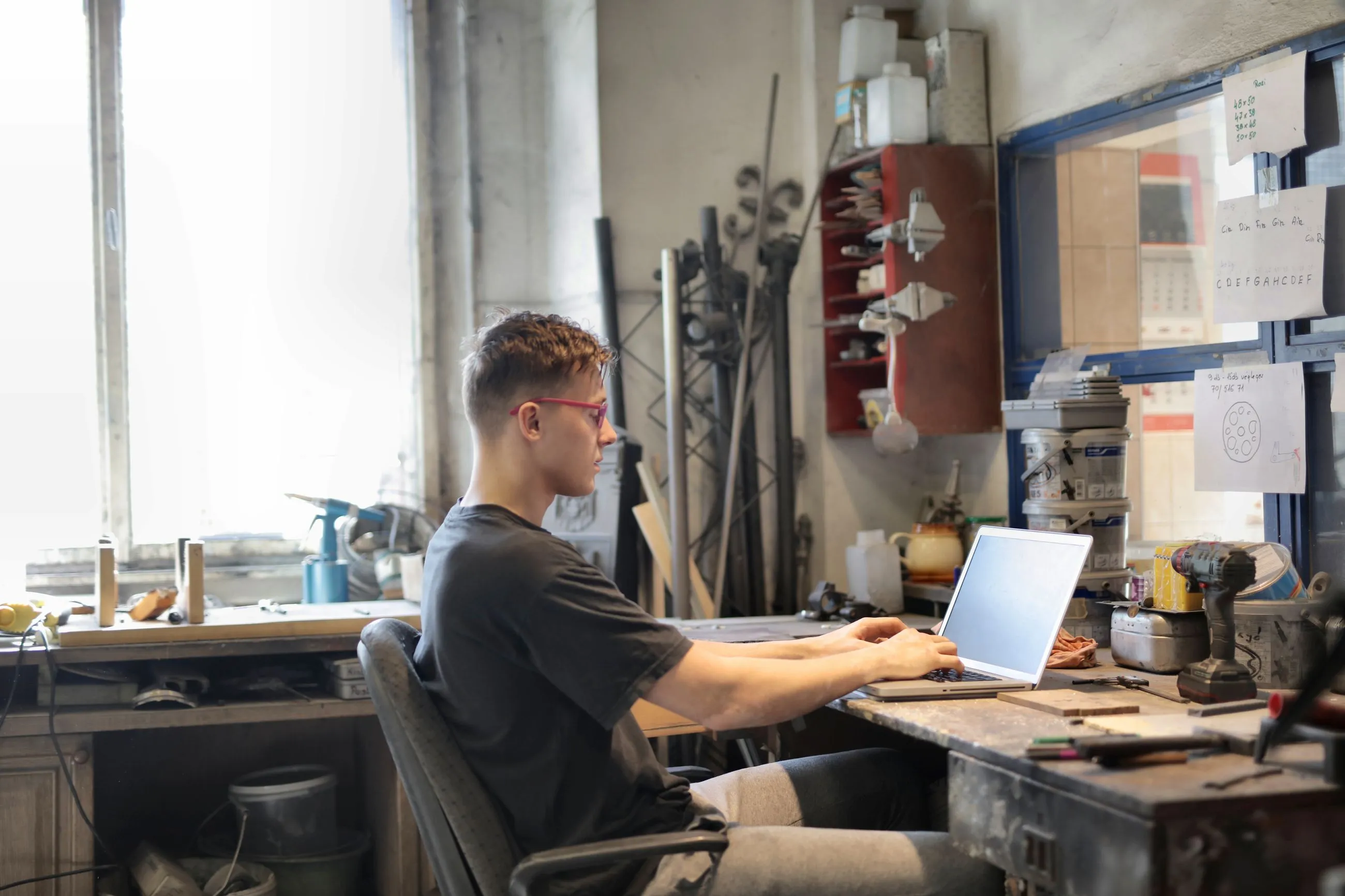 Joven trabajando con un portátil en un taller rodeado de herramientas