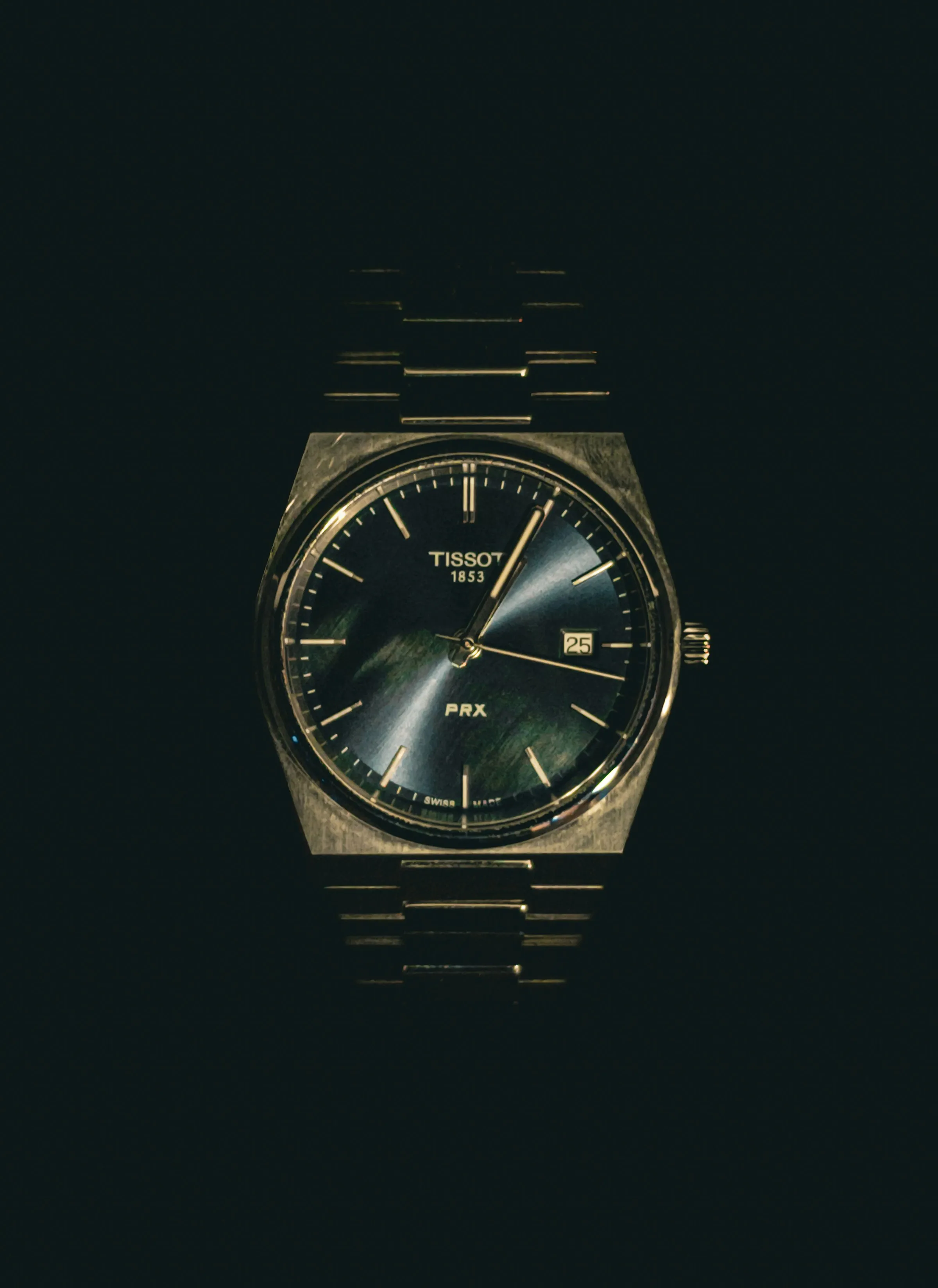 Tissot PRX de esfera oscura y brazalete integrado emergiendo de la penumbra